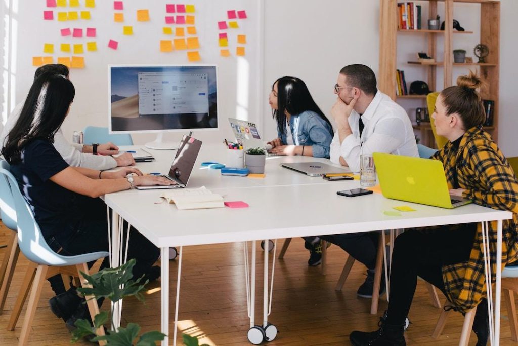 A sales team sitting at a white table looking at a computer screen, learning about effective sales leadership.